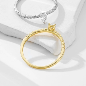 Macro shot of silver and gold pear-cut zircon rings on a white textured stone base