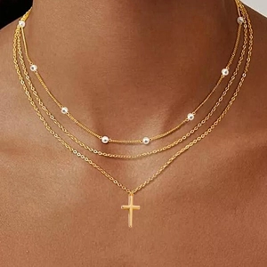 Three-layer gold necklace with white pearls and a polished cross pendant on model