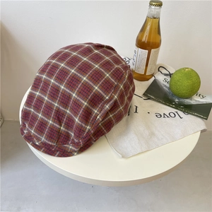 Vintage red plaid newsboy cap in Scottish tartan cotton on a minimalist white table