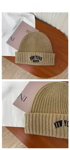 Detail of camel rib-knit beanie with New York embroidery on a warm wooden background