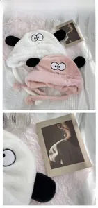 Close-up of plush puppy earflap hats in white and pink featuring cute cartoon eyes