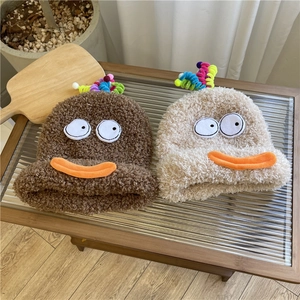 Plush winter beanies with cartoon eyes and colorful pompoms on a wooden table