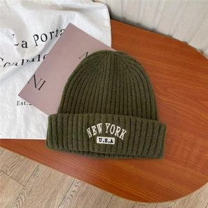 Olive green knit beanie featuring New York USA embroidery on a flat lay wooden surface