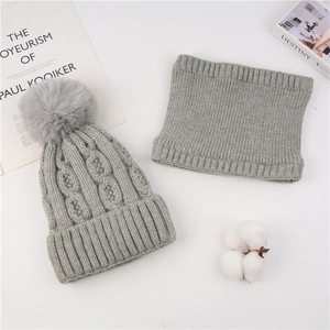 Detail of light gray cable knit beanie with fluffy pompom and matching neck warmer scarf