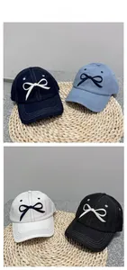 Detail showing four colors of embroidered bow baseball caps on a woven straw mat