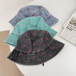 Three embroidered butterfly denim bucket hats in light blue, teal, and dark grey on a table