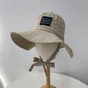 Green and pink checkered sun hat with black label and windproof strap on model stand