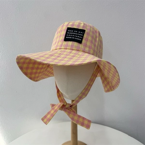 Pink and yellow checkered sun hat with wide brim and chin strap on a white stand
