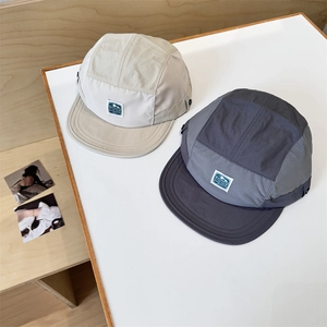 Quick-dry five-panel camper hats in cream and dark grey on a minimalist wooden background