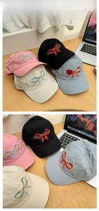 Close-up of baseball caps with bow embroidery and text detail in four soft colors