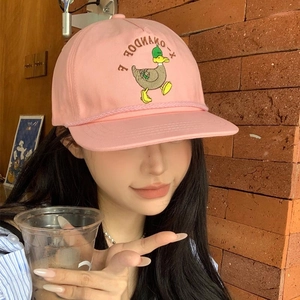 Pink flat brim baseball cap with duck embroidery worn by model in a rustic setting