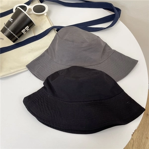 Flat lay of cotton bucket hats in black and dark grey on white table with fashion props