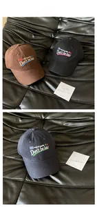 Detailed view of Don't Be Late embroidery on cotton baseball caps in brown, black and navy
