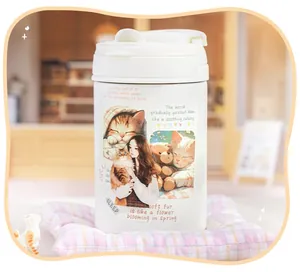 Close-up of a white insulated mug decorated with cute kitten and girl themed stickers