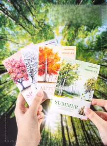 Four seasons trees stickers held against a blurred forest background for scrapbooking