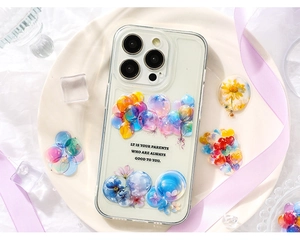 Custodia per iPhone trasparente con palloncini colorati e fiori su un piatto bianco