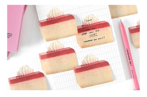 Close-up of strawberry cream cake shaped sticky notes on a white grid paper background
