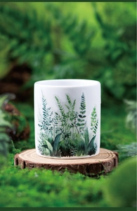 Detail of a white ceramic mug featuring green fern botanical prints on a wood block