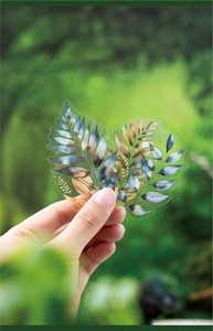 Detailed view of semi-transparent leaf-shaped PET stickers held in a forest setting