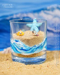 Detail of creative blue wave stickers on glass cup with miniature summer beach scene inside