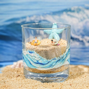 Ocean wave pattern decorative glass cup with miniature figures on a sandy beach setting
