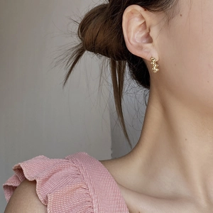 Close-up of a gold oval bead earring with a twisted texture worn on a model ear
