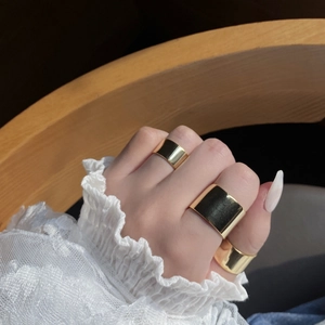 Detailed view of three-piece set glossy gold wide band rings on model's fingers