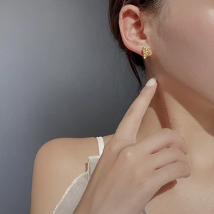 Close-up of gold heart stud earring with hammered texture worn by a model