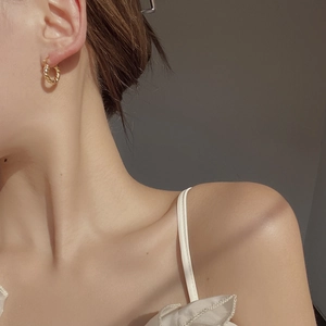 Close-up of a woman wearing gold twisted rope hoop earrings in elegant natural lighting