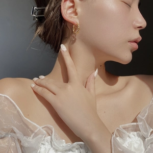 Close-up of golden Chaine d'Ancre style earrings worn by a model in natural light