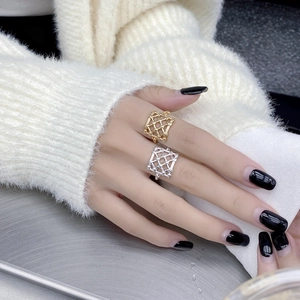 Close-up of gold and silver square mesh rings worn against a white knit background