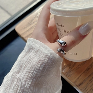 Polished silver teardrop ring shown on hand against a cozy coffee scene background