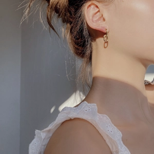 Close-up of geometric 18K gold plated chain link earrings on a model with warm lighting