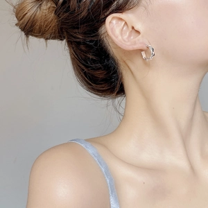 Close-up of a silver twisted rope C-shaped hoop earring worn by a female model