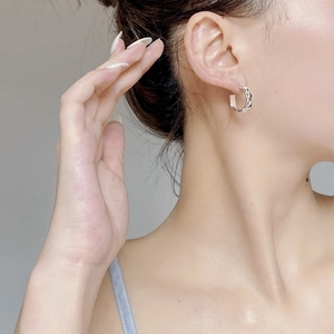Macro shot of silver twisted hoop earring with woven texture shown on a female ear