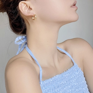 Close-up of gold C-shaped twisted earrings with woven metal texture on a model