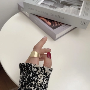 Close-up of minimalist wide gold band ring worn on hand with red nail polish