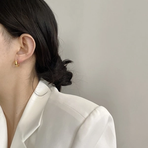 Gros plan détaillé de créoles dorées style croissant portées avec un costume blanc