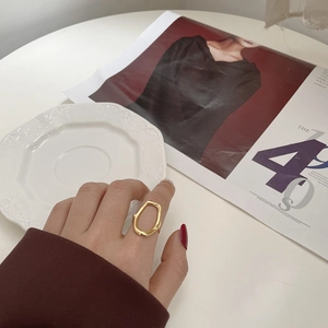 Detailed view of a golden irregular hollow ring styled on a model's hand with accessories