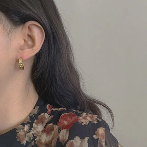 Close-up of a model wearing a textured golden C-shaped earring with tank chain pattern