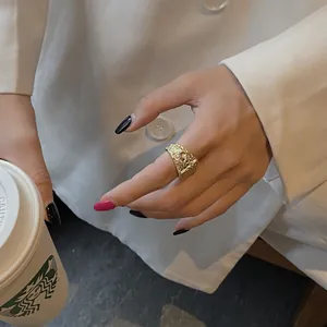 Detail of a gold textured square ring showing a crinkled metal surface on a hand