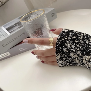 Detail of wide gold irregular textured ring worn while holding a hammered glass