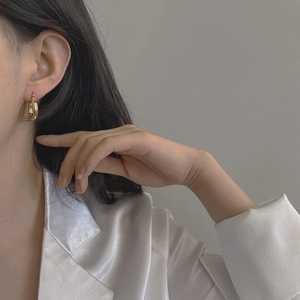 Close-up of minimalist chunky gold hoop earrings worn with a white satin blazer