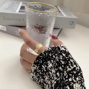 Detailed view of an irregular hammered gold wide band ring worn with a luxury glass
