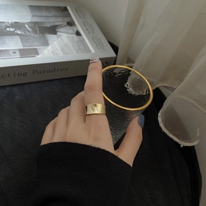 Macro view of wide gold-plated ring with irregular hammered texture on model's finger