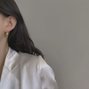 Close-up of elegant gold hoop earrings worn by a model in a white silk suit
