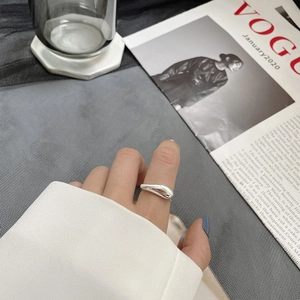 Vue macro d'une bague goutte irrégulière minimaliste en argent portée sur l'index stylé