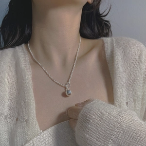 Close-up of S925 sterling silver ball pendant necklace on model with knitwear