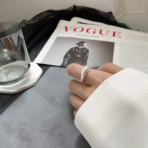 Bague irrégulière en métal liquide argenté sur main avec fond de magazine de mode