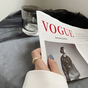 Gros plan d'une bague chevalière géométrique en or portée à l'index avec un magazine de mode